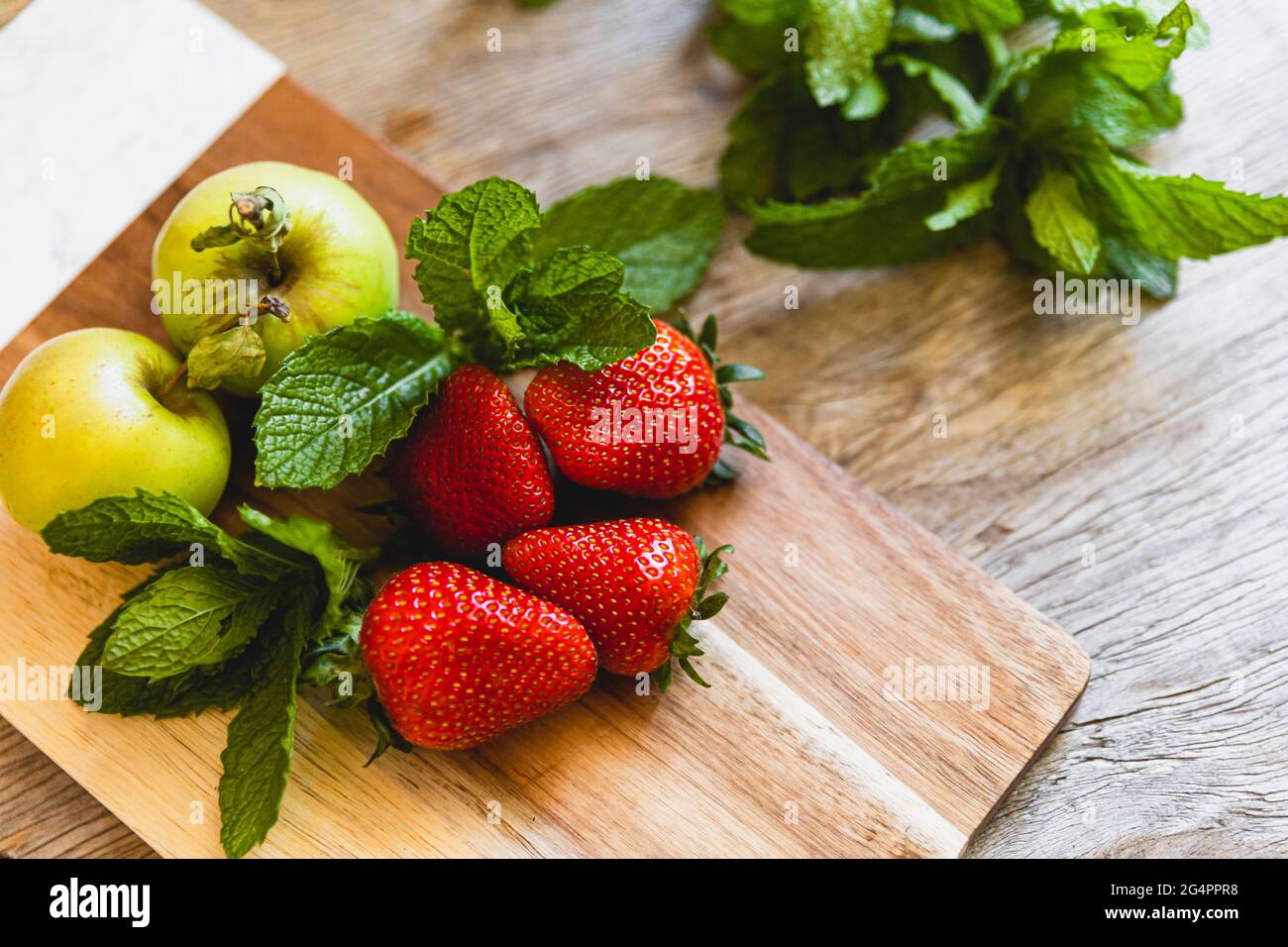 Des pommes vertes, de la menthe et des fraises sur une planche à découper en préparation culinaire. Banque D'Images