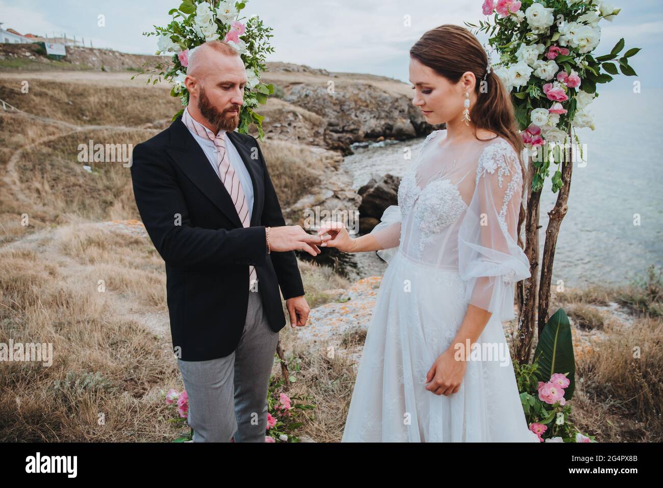 Les jeunes femmes vêlées d'une robe blanche mettent un anneau sur le doigt d'un homme dans un costume. Cérémonie de mariage. Banque D'Images