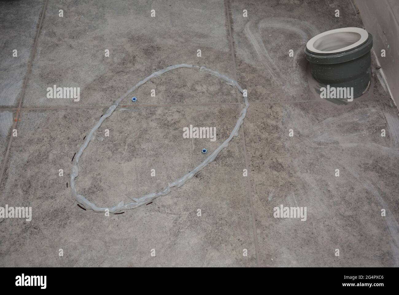 Installation d'un bol de toilettes sur un sol carrelé dans une salle de bains. Appliquer de la colle sur un sol carrelé pour coller un siège de toilettes. Banque D'Images