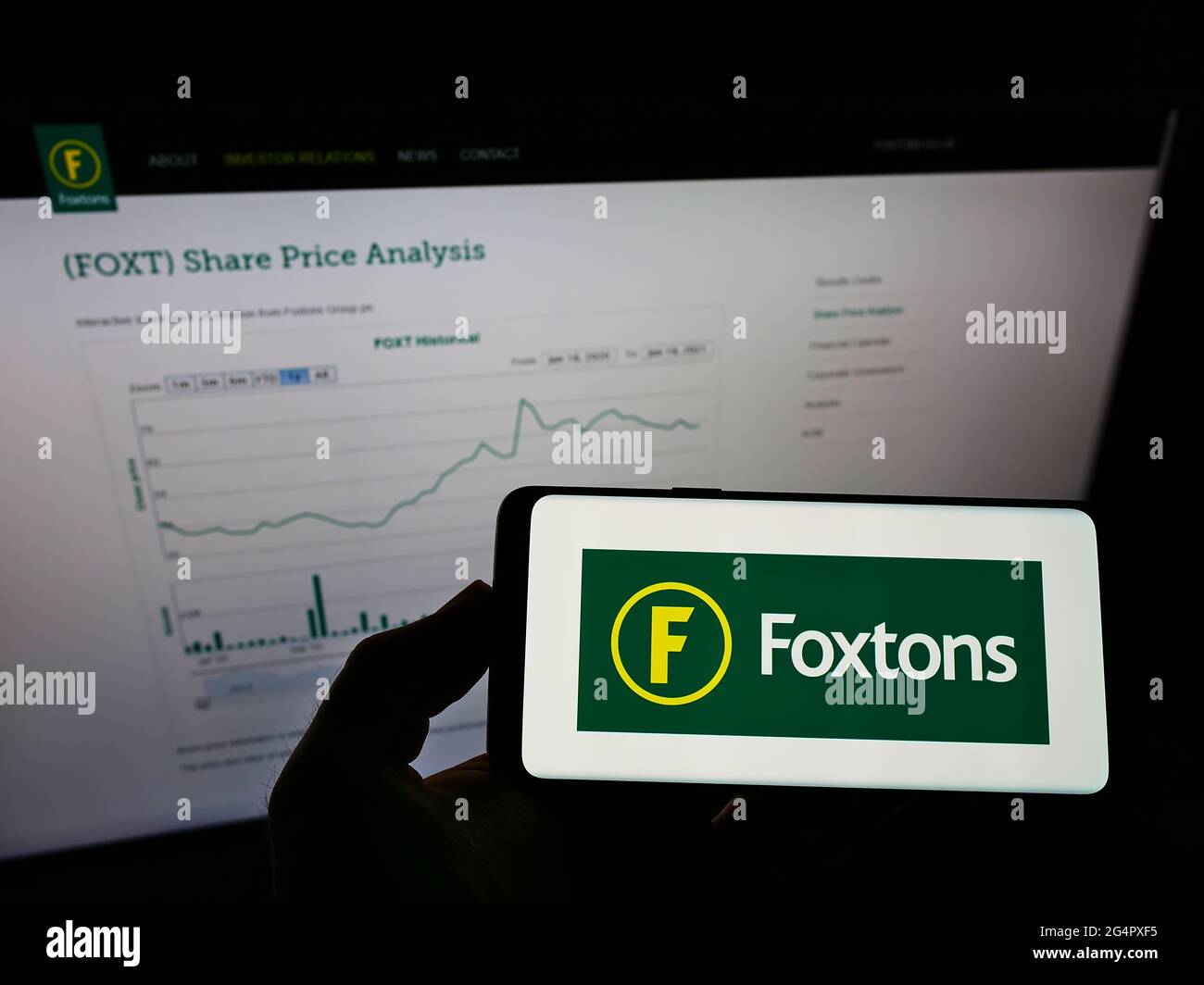 Personne tenant un téléphone portable avec le logo de l'agence immobilière britannique Foxtons Group plc sur l'écran en face de la page Web d'affaires. Mise au point sur l'affichage du téléphone. Banque D'Images