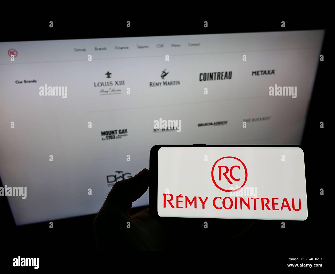 Personne tenant un smartphone avec le logo de la société française de spiritueux Rémy Cointreau S.A. sur écran devant le site. Mise au point sur l'affichage du téléphone. Banque D'Images