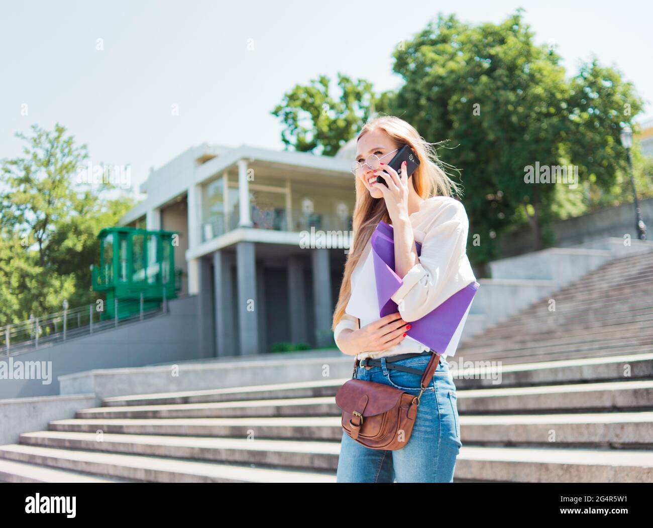 Jeune femme caucasienne étudiant en vêtements décontractés avec l'esse dans un dossier parlant au téléphone en descendant les escaliers Banque D'Images