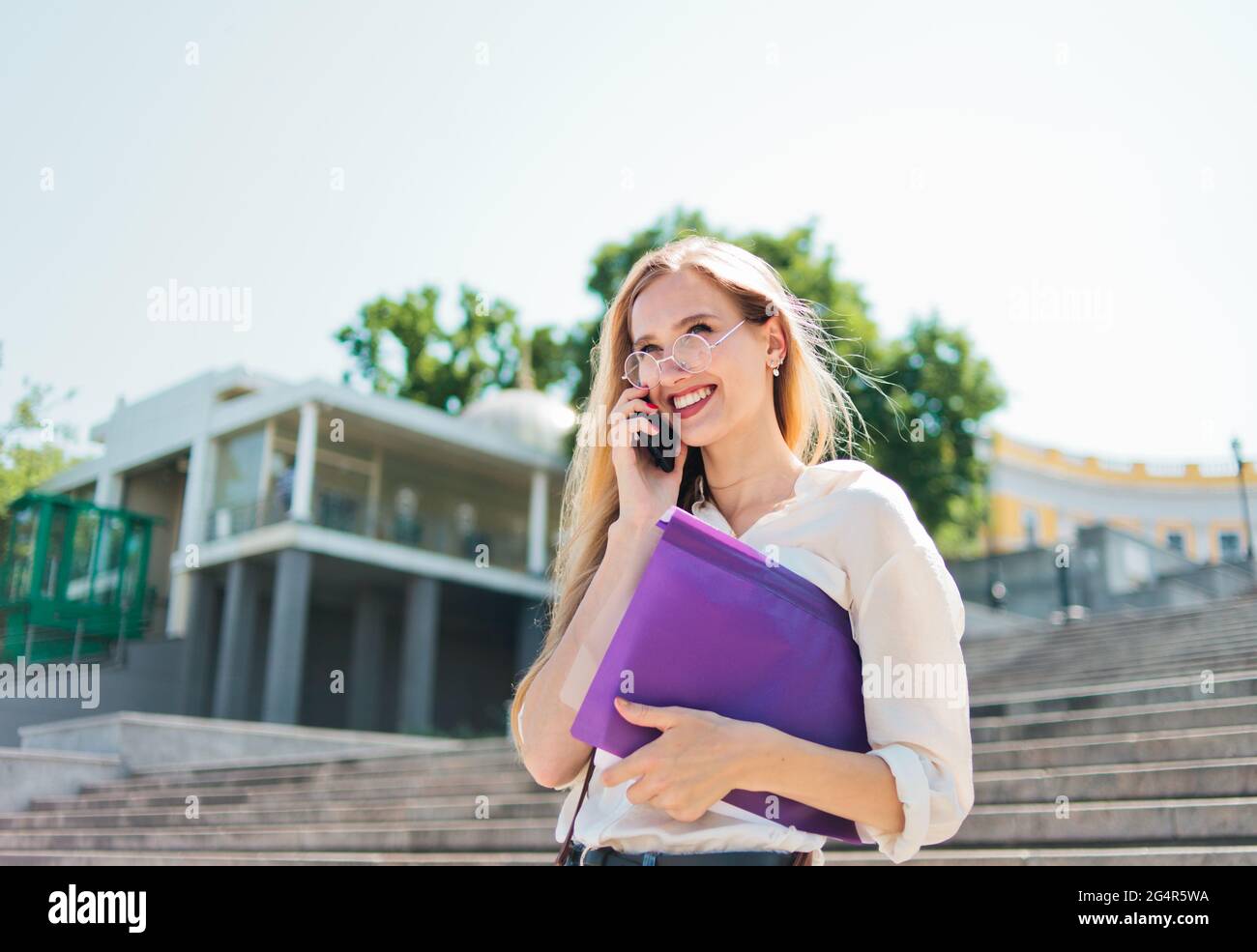 Jeune femme caucasienne étudiant en vêtements décontractés avec l'esse dans un dossier parlant au téléphone en descendant les escaliers Banque D'Images