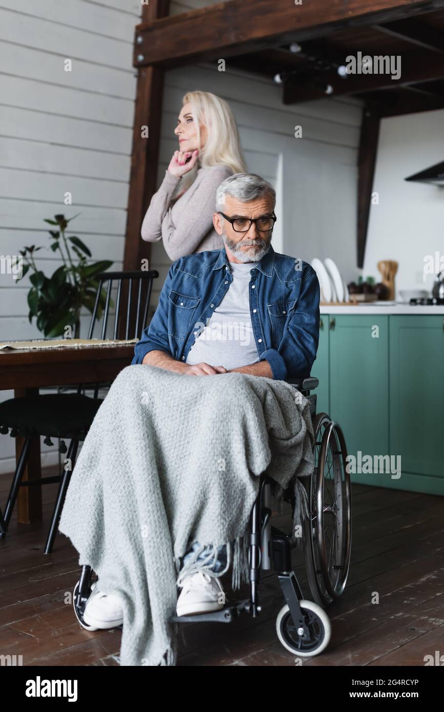 Triste homme handicapé en fauteuil roulant qui regarde loin près de la femme à la maison Banque D'Images