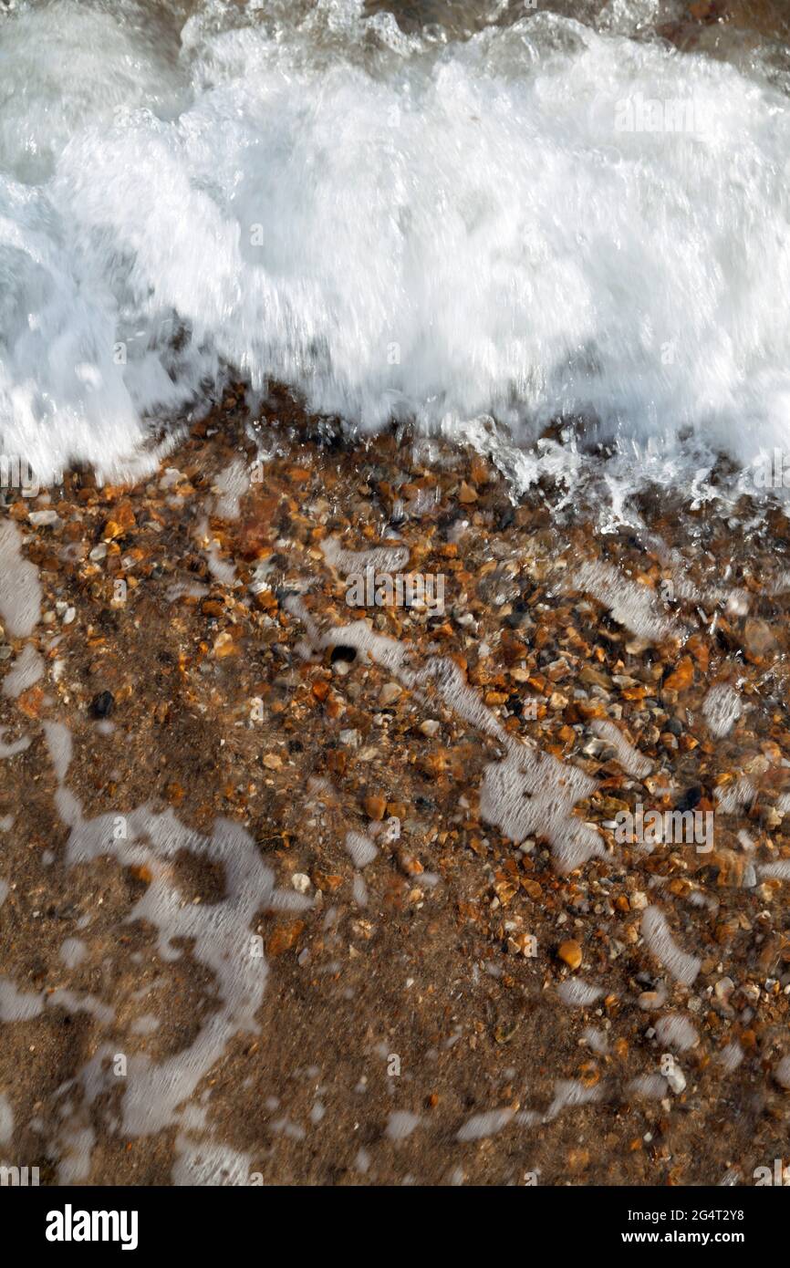 Gros plan de petites vagues se brisant sur la plage, créant des bulles et de la mousse Banque D'Images