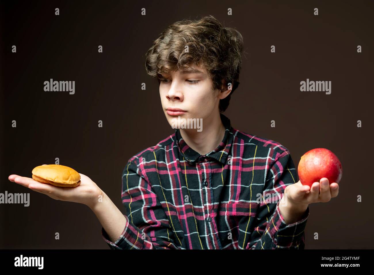 jeune homme tenant et choisissant entre pomme ou hamburger Banque D'Images