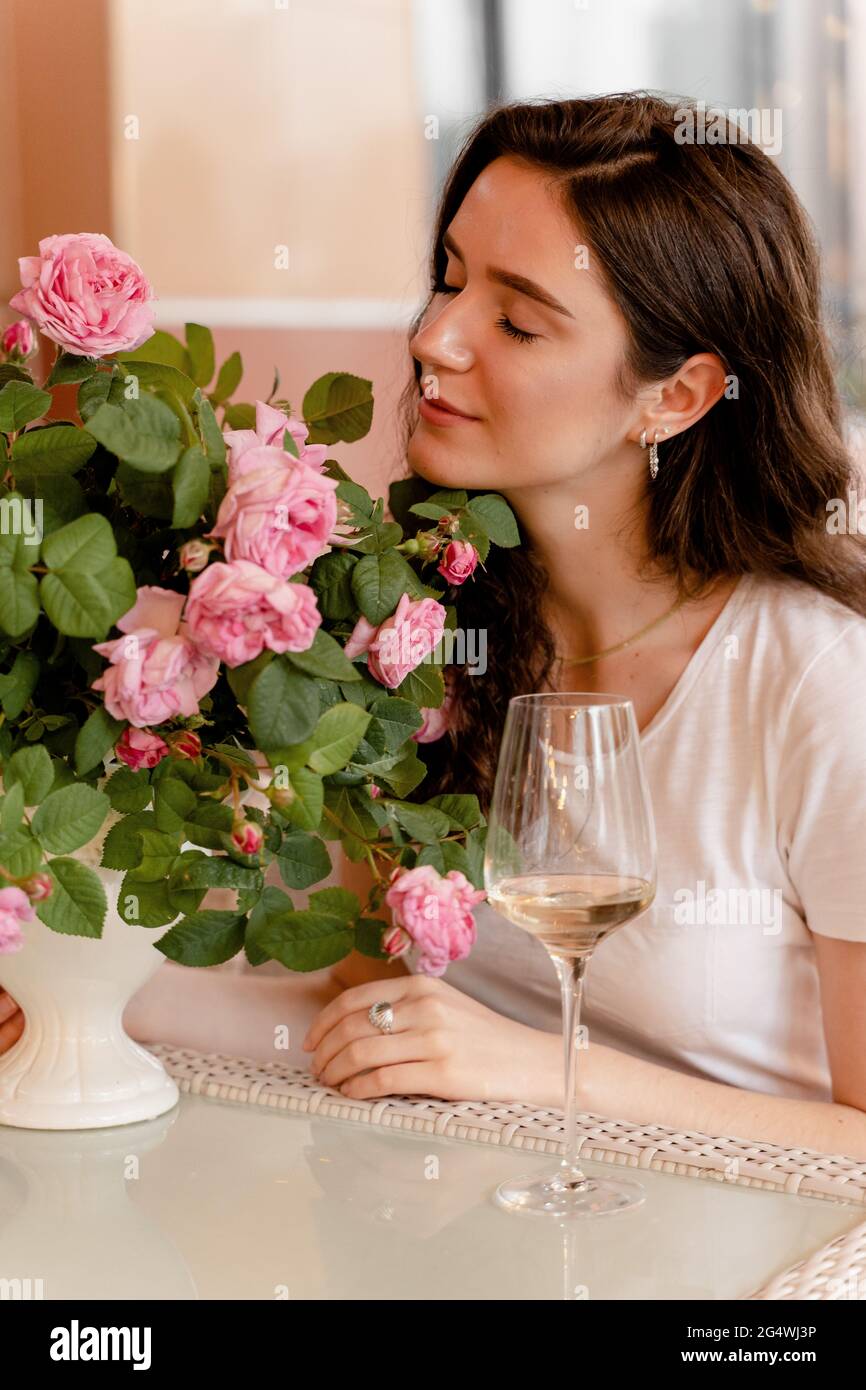 Femme rêvant avec un verre de vin blanc alcoolisé dans un café en terrasse d'été et bouquet de roses sur la table Banque D'Images