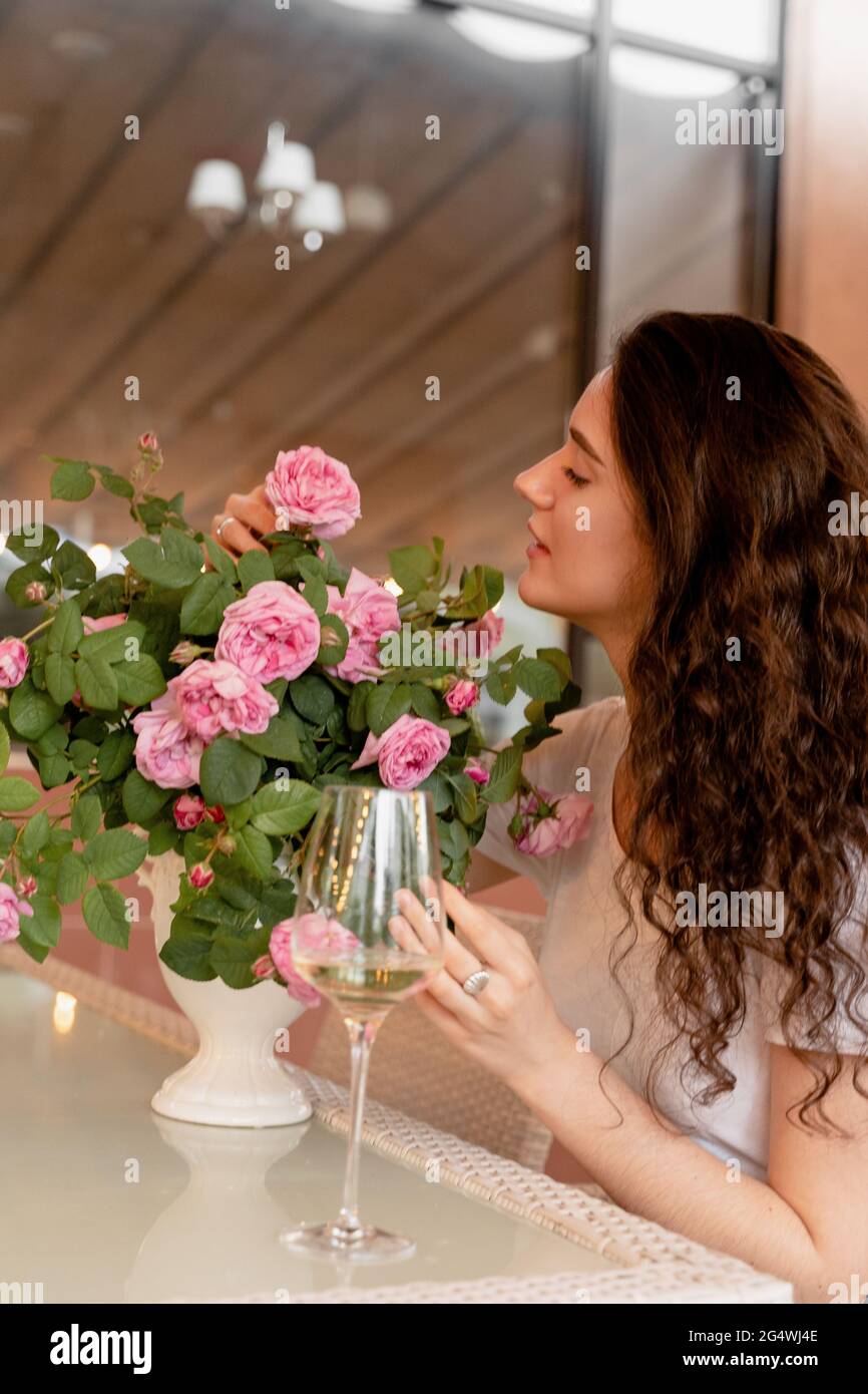 Femme rêvant avec un verre de vin blanc alcoolisé dans un café en terrasse d'été et bouquet de roses sur la table Banque D'Images