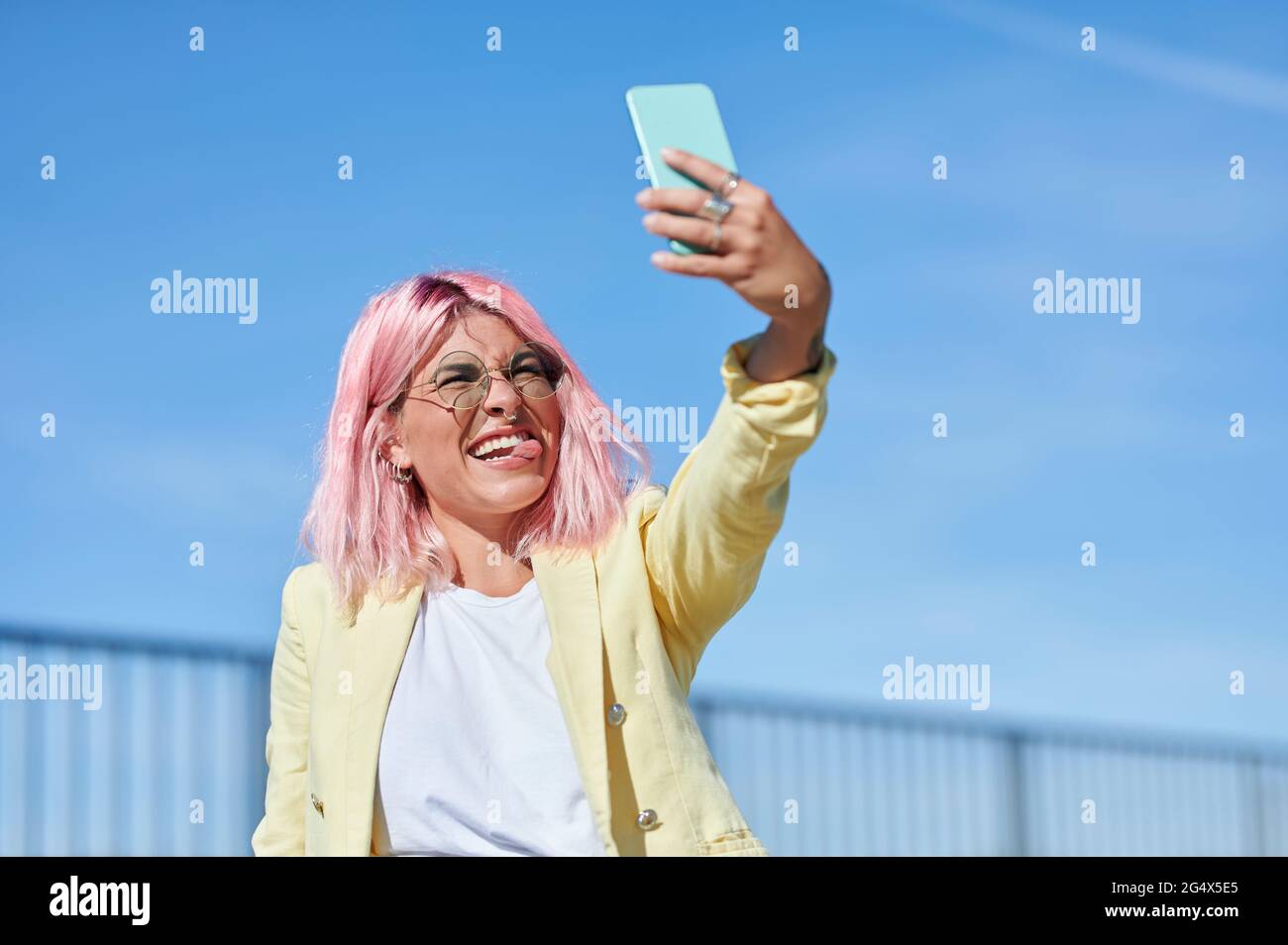 Jeune femme qui colle la langue tout en prenant le selfie à travers le smartphone par beau temps Banque D'Images