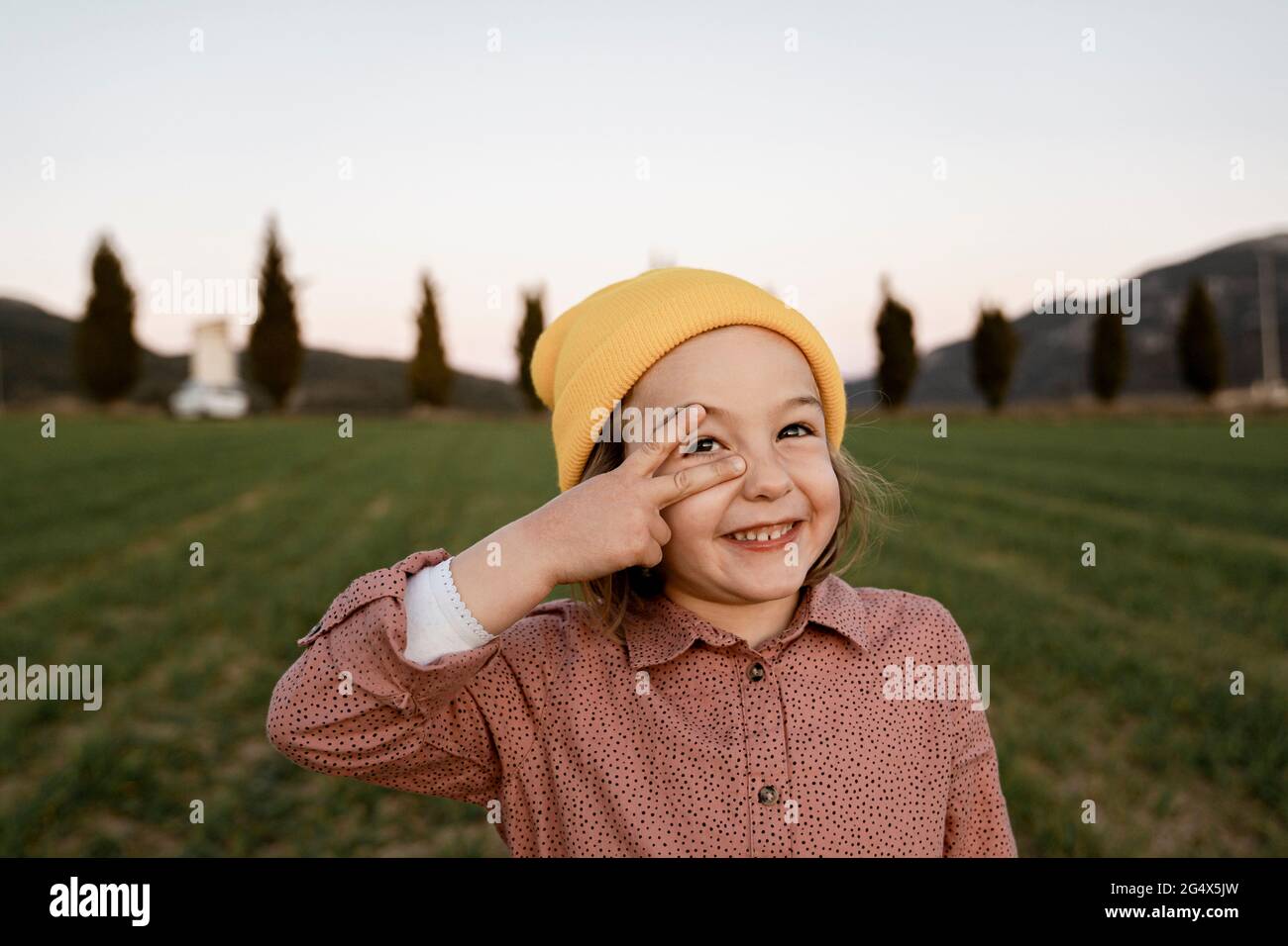Fille souriante portant un chapeau en tricot faisant signe de paix tout en regardant loin Banque D'Images