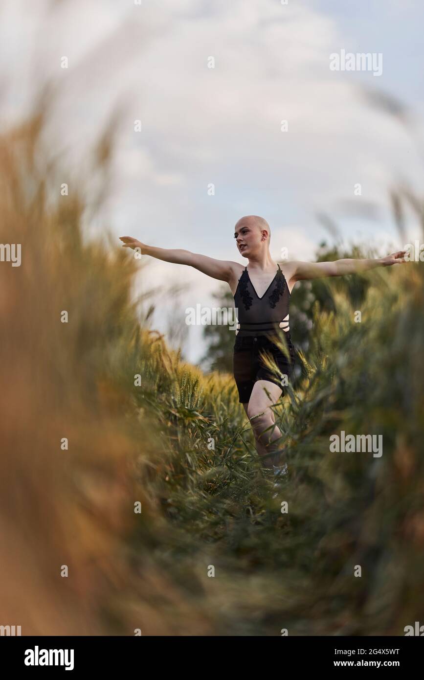 Femme bald transgenre vêtue de robe noire marchant avec les bras étirés dans le champ agricole Banque D'Images