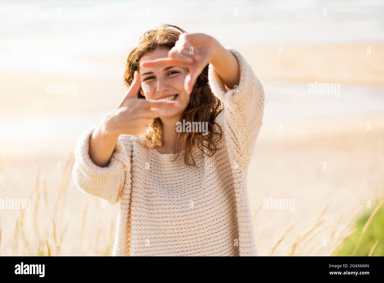 Bonne femme regardant à travers le cadre de doigt à la plage pendant la journée ensoleillée Banque D'Images
