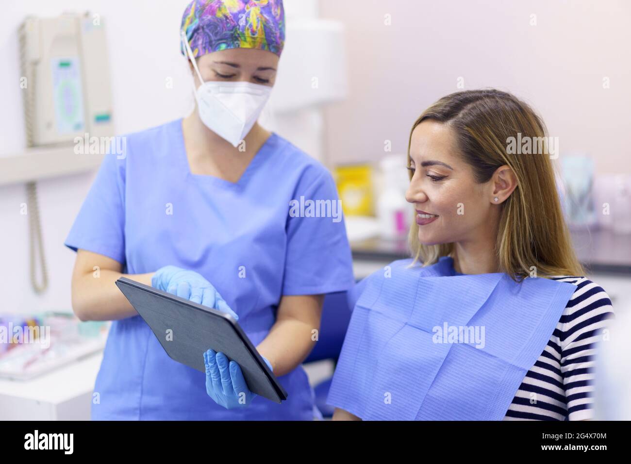 Dentiste femme portant un masque de protection montrant un comprimé numérique au patient à la clinique médicale Banque D'Images