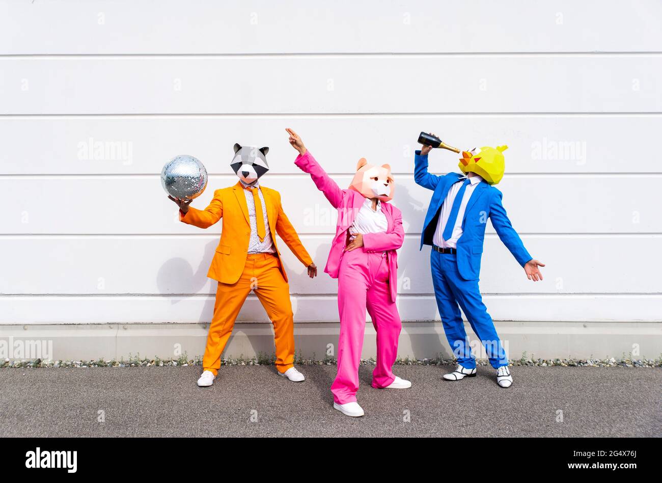 Trois personnes portant des costumes vibrants et des masques pour animaux faisant la fête devant le mur blanc Banque D'Images