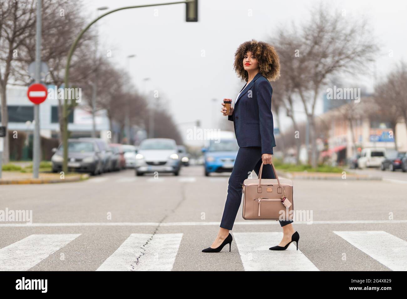 Femme d'affaires bien habillée avec porte-monnaie traversant la route en ville Banque D'Images