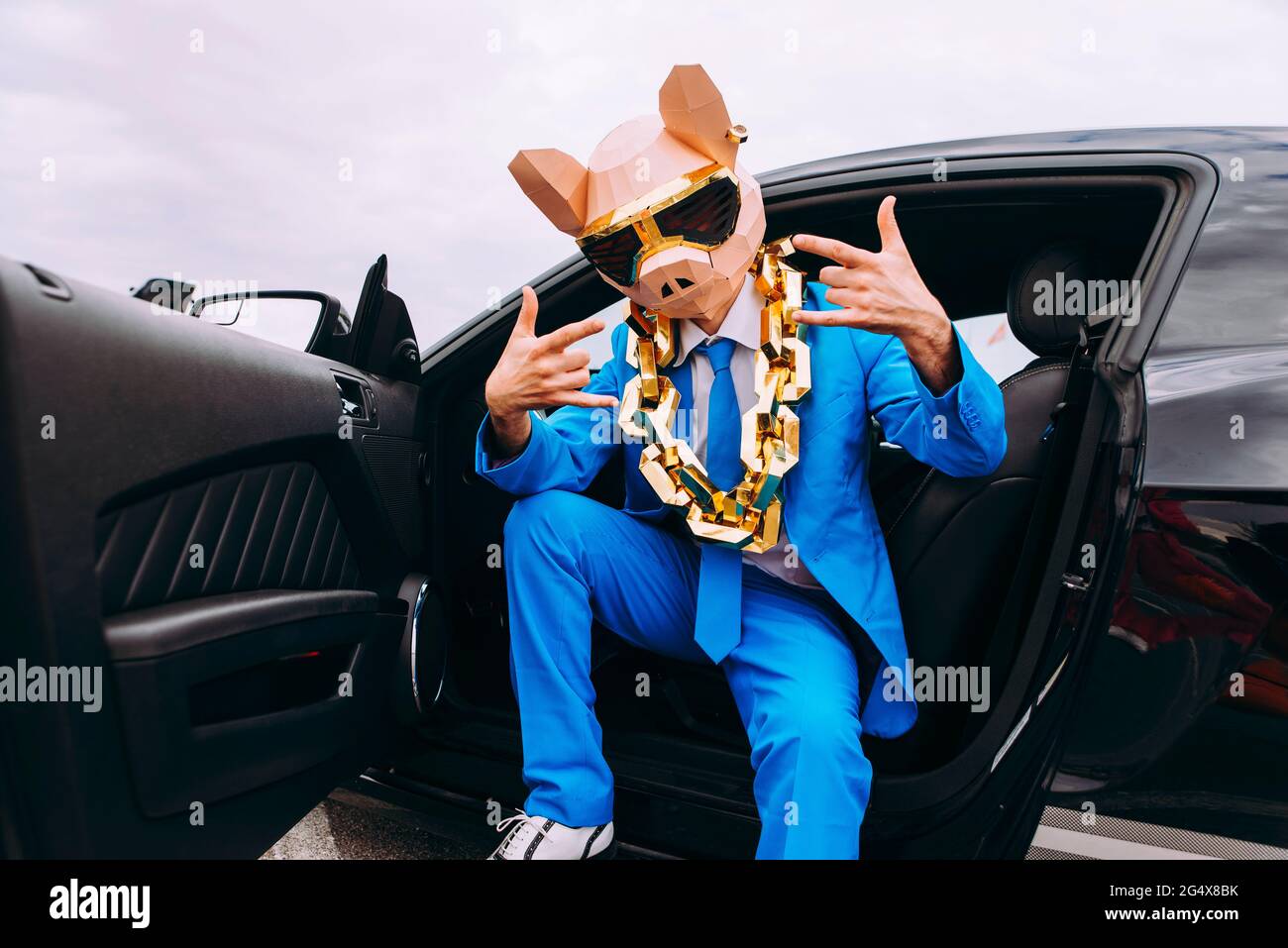 Drôle de caractère dans le masque d'animal et bleu costume d'affaires assis dans la voiture et gesturant Banque D'Images