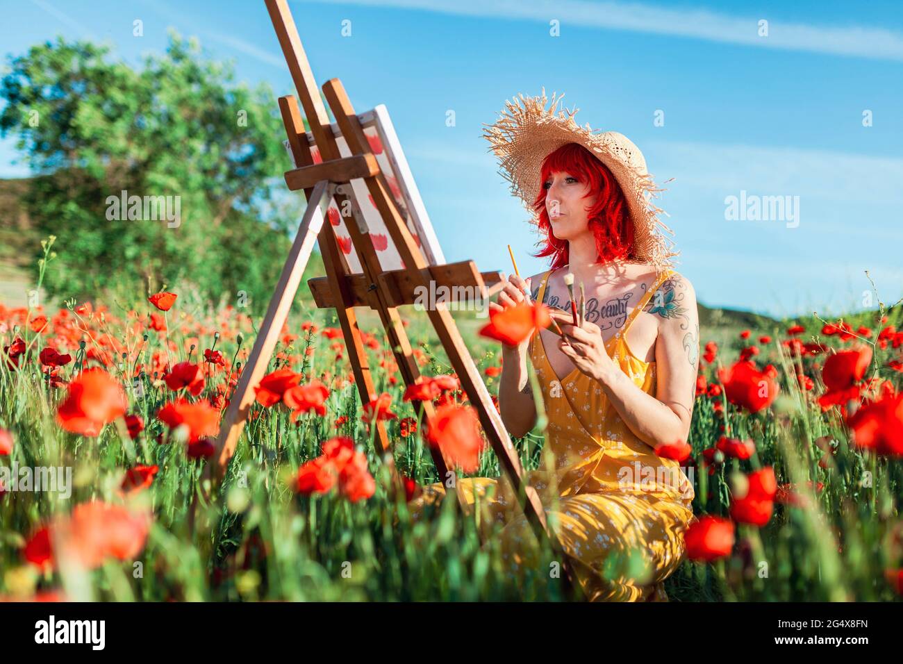 Femme avec des cheveux teints rouge peinture sur toile au champ de pavot Banque D'Images