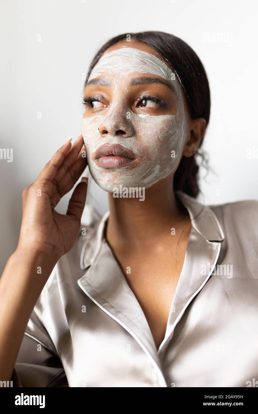 Femme regardant loin en touchant le visage avec un masque de beauté à la maison Banque D'Images