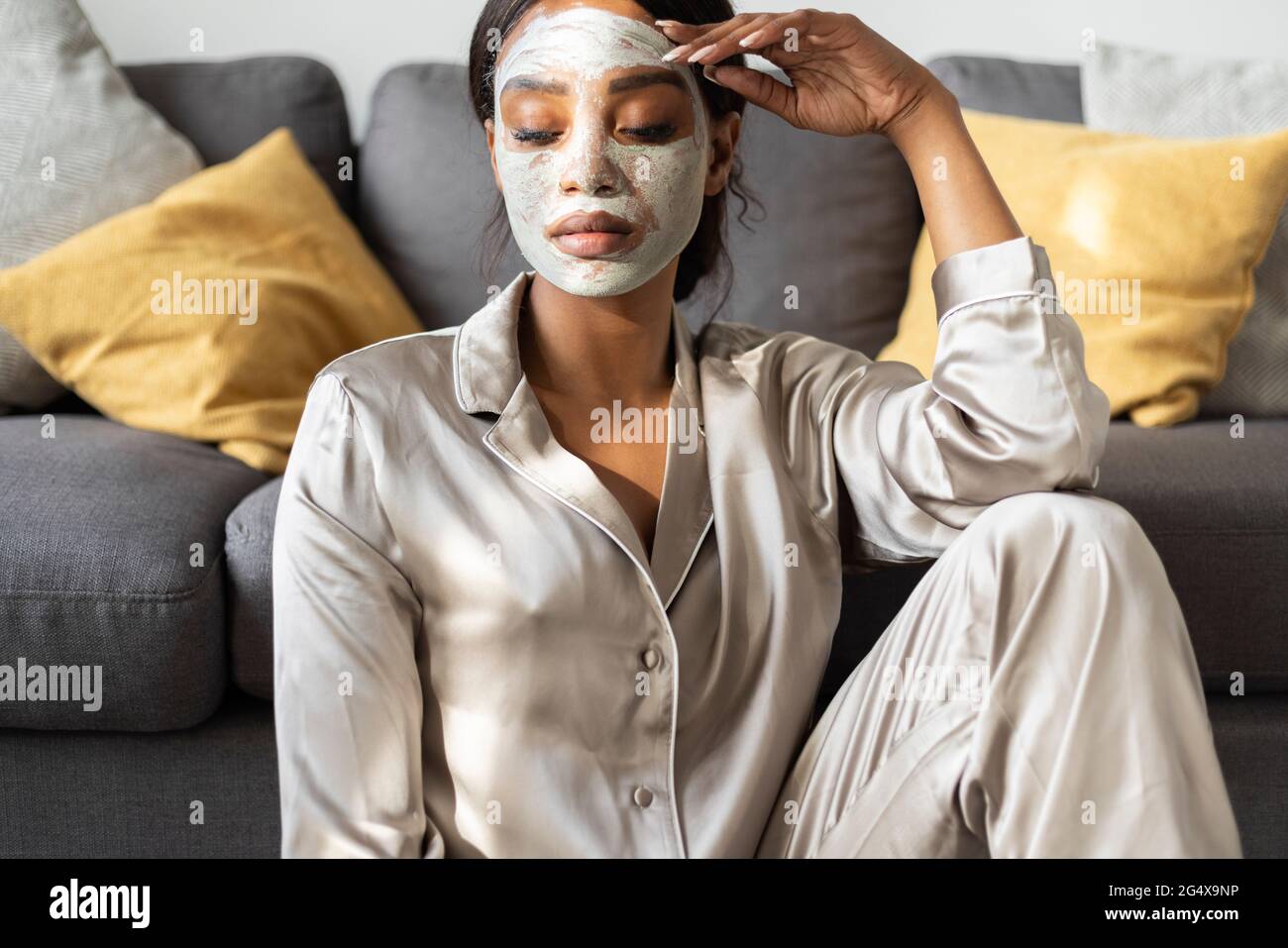 Femme sérieuse avec masque facial de beauté assis dans le salon à la maison Banque D'Images