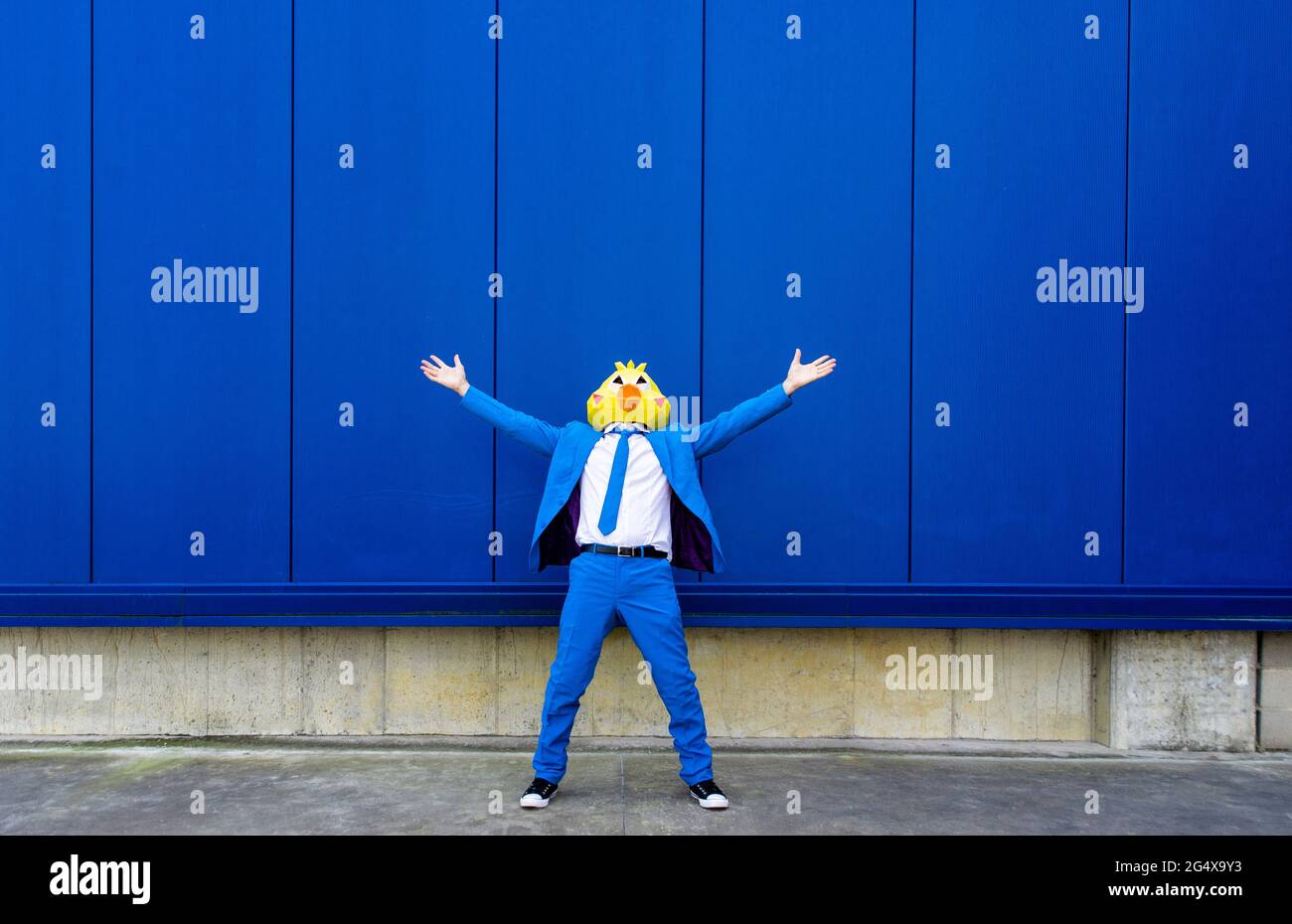 Homme portant un costume bleu vif et un masque d'oiseau debout à l'extérieur avec les bras relevés Banque D'Images