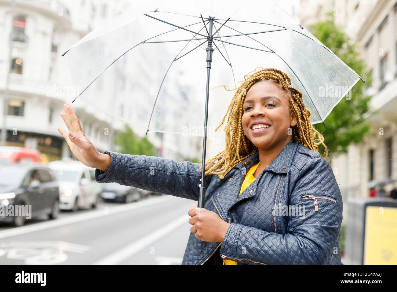 Une femme heureuse avec des tresses tenant un parapluie tout en hélant un taxi dans la ville Banque D'Images
