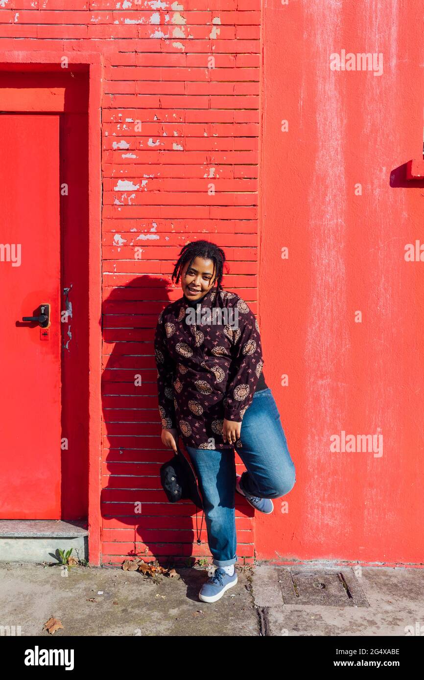 Femme souriante tenant un chapeau en face du bâtiment rouge Banque D'Images