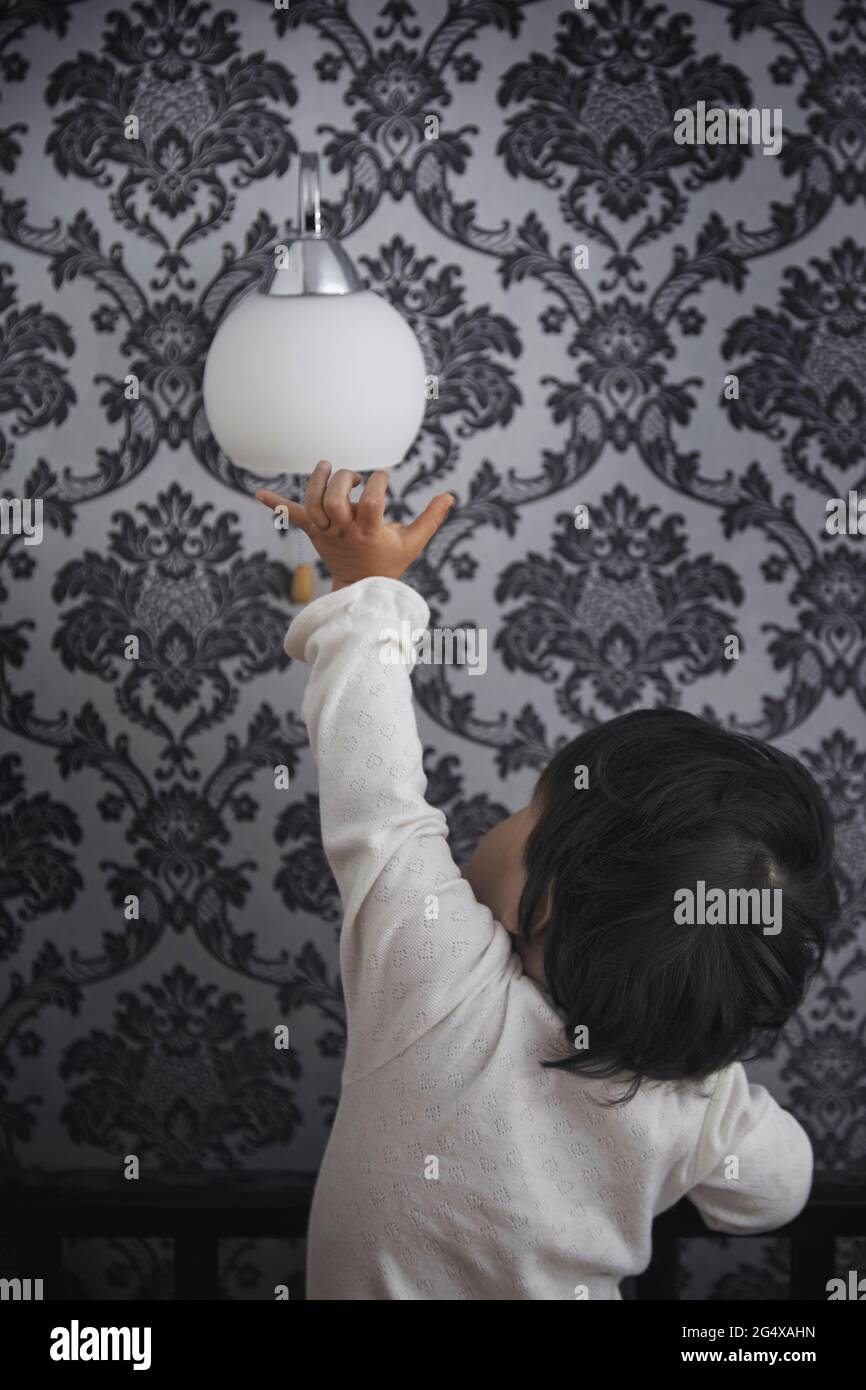 Bébé fille touchant la lampe électrique sur le mur à la maison Banque D'Images