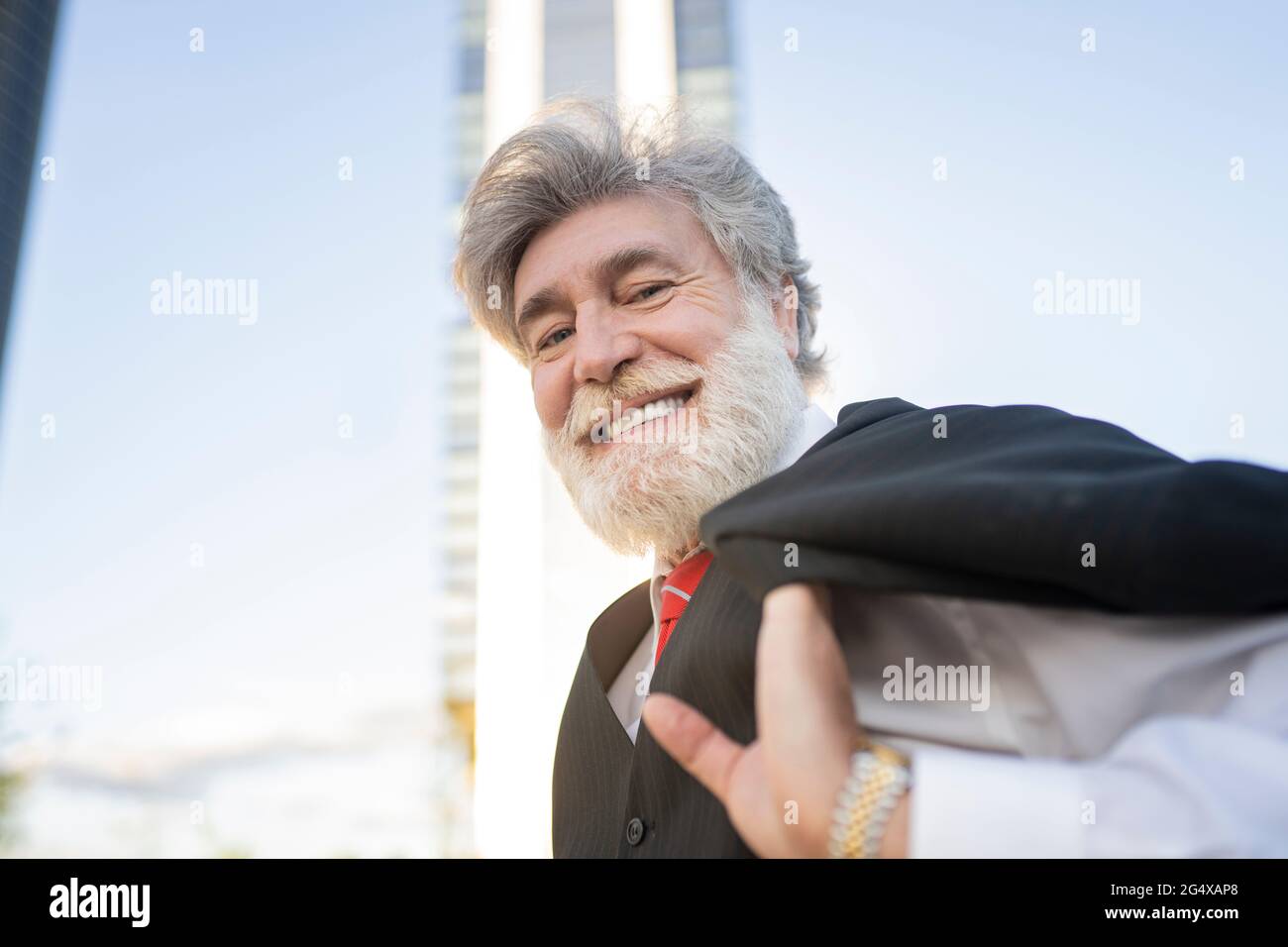 Homme d'affaires souriant portant une veste de costume sur l'épaule en ville Banque D'Images