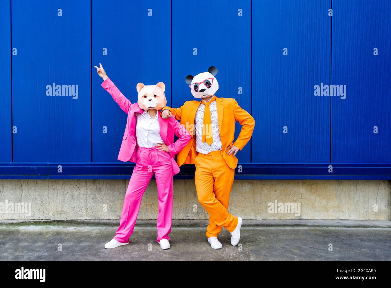 Homme et femme portant des costumes vibrants et des masques d'ours debout ensemble contre le mur bleu Banque D'Images