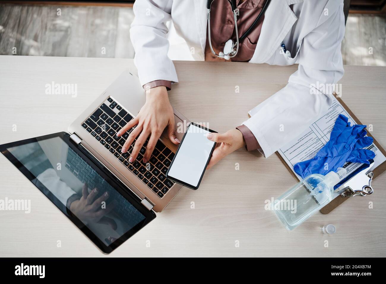 Femme médecin tenant un smartphone tout en utilisant un ordinateur portable au bureau Banque D'Images