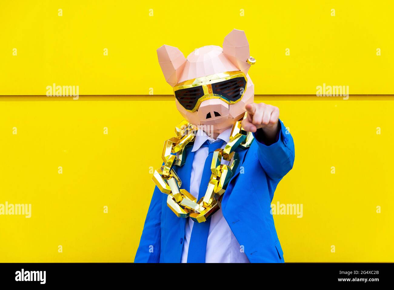 Homme portant un costume bleu vif, un masque de porc et une grande chaîne dorée pointant vers l'appareil photo Banque D'Images