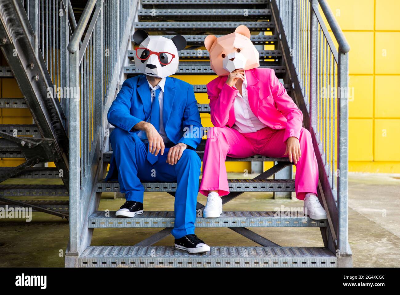 Homme et femme portant des costumes vibrants et des masques d'ours assis ensemble sur des escaliers métalliques Banque D'Images