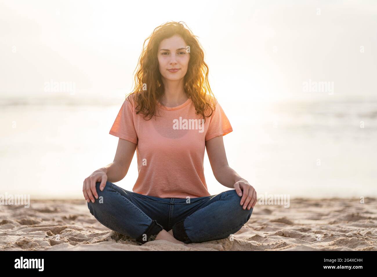 Jeune femme aux pieds croisés assise sur le sable à la plage Banque D'Images