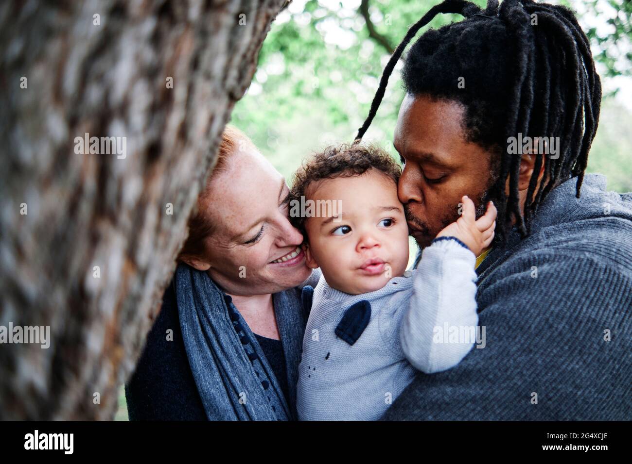 Une famille heureuse embrasse son mignon au parc Banque D'Images