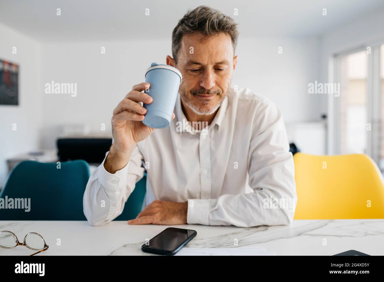 Homme indépendant tenant une tasse de café réutilisable dans l'îlot de cuisine Banque D'Images