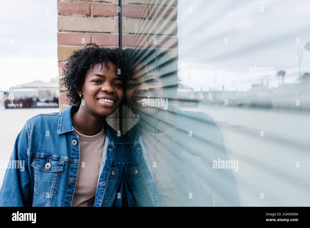 Femme Afro souriante penchée sur une fenêtre en verre Banque D'Images
