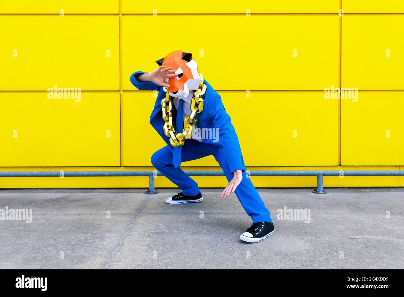 Homme portant un costume bleu vif et un masque tigre debout en position de combat devant le mur jaune Banque D'Images