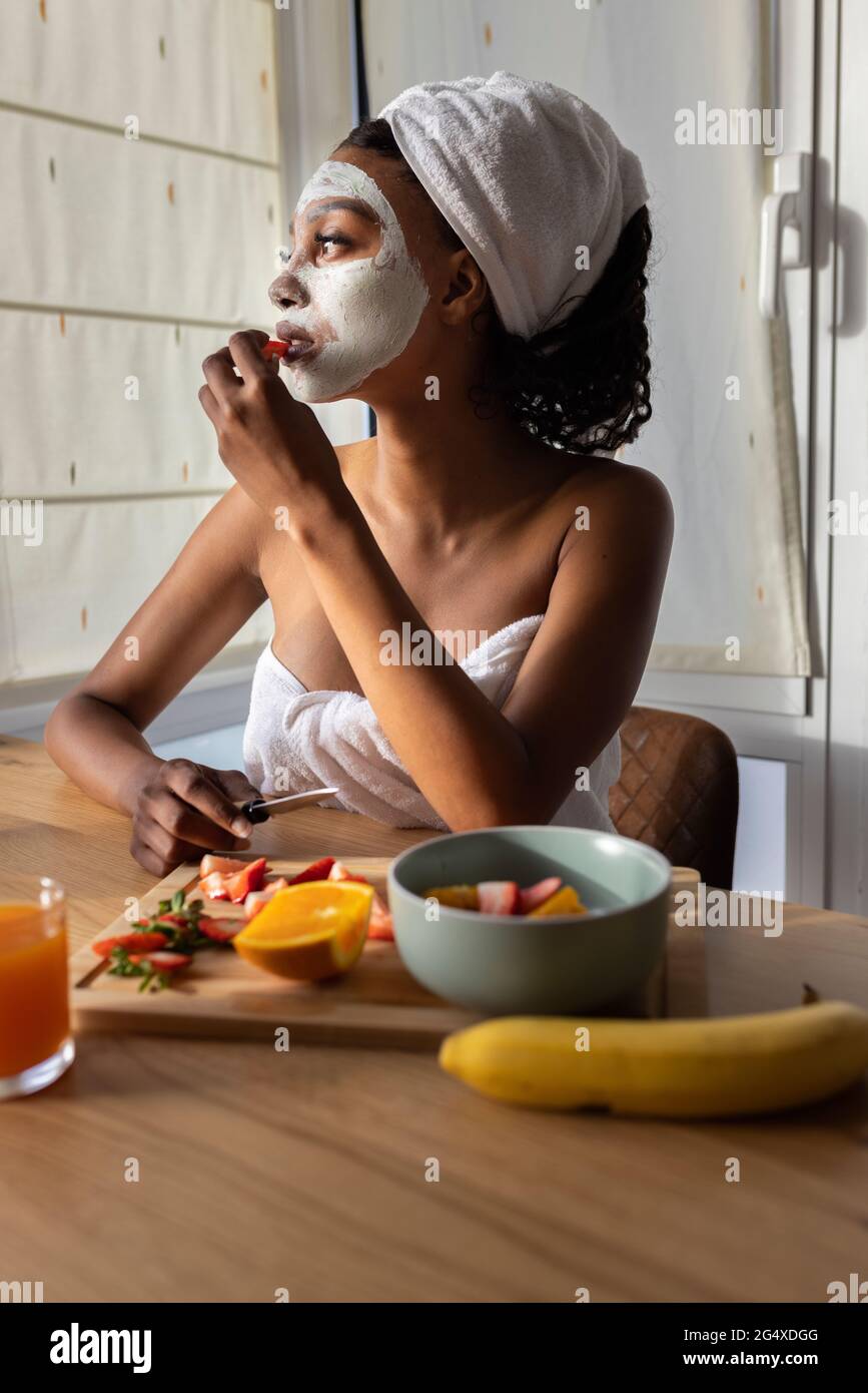 Femme avec masque facial prenant le petit déjeuner à la maison Banque D'Images