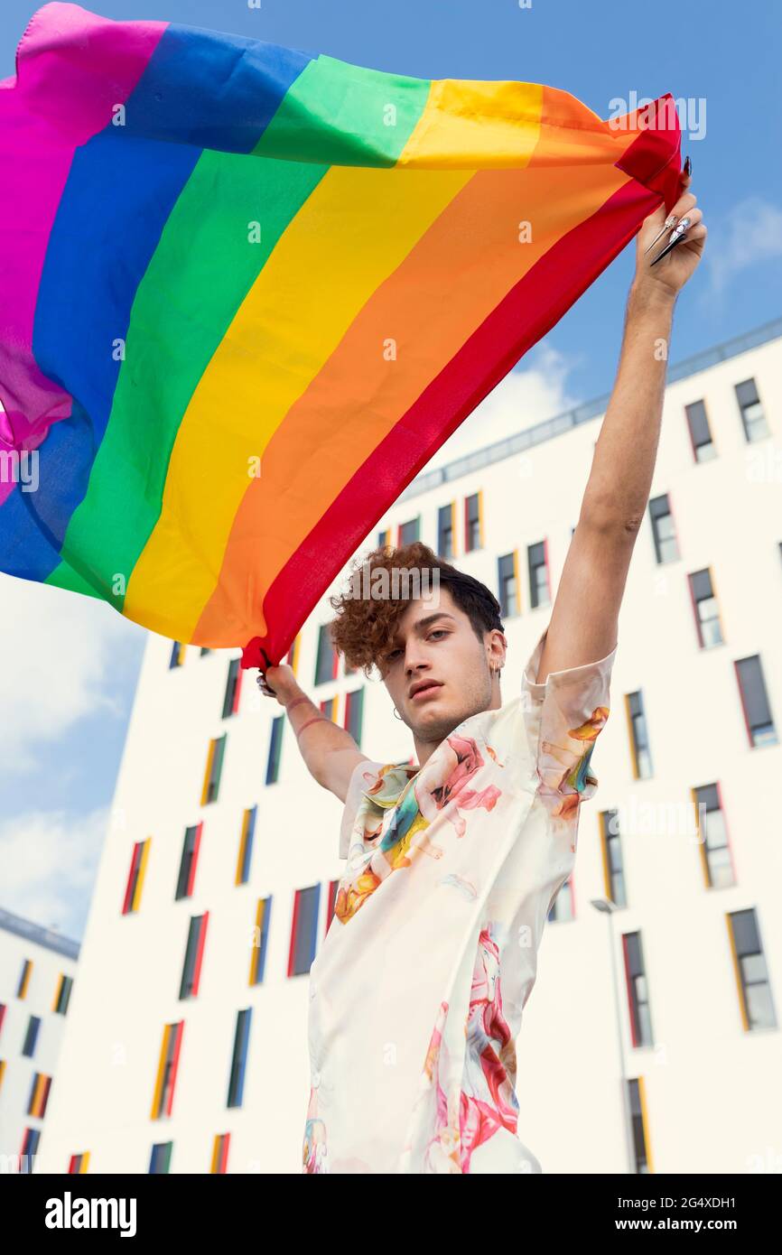 Jeune homme soufflant le drapeau arc-en-ciel devant le bâtiment Banque D'Images
