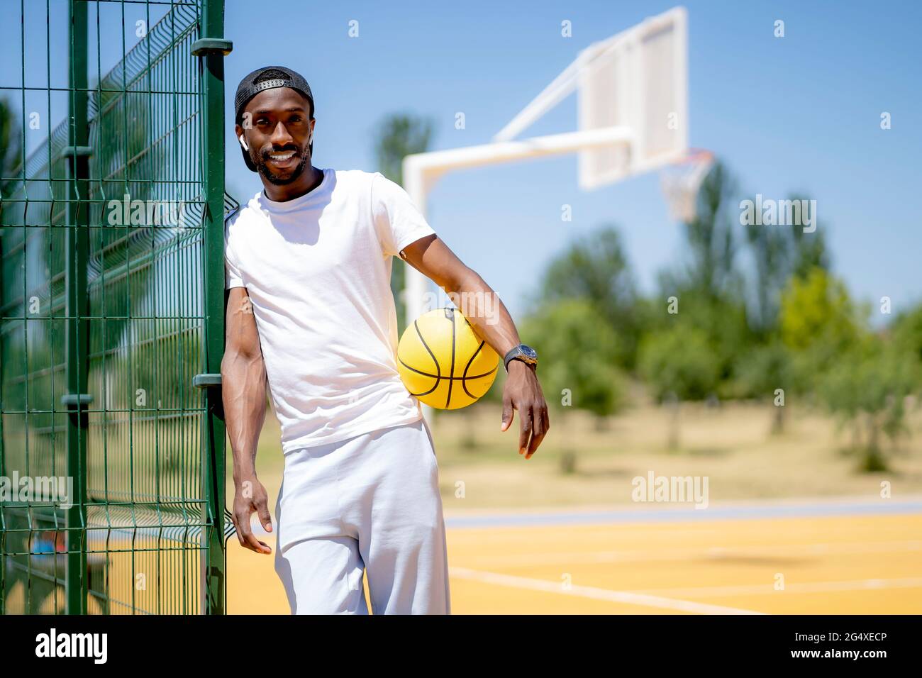 Homme tenant un ballon de basket-ball en se tenant sur un terrain de sport par beau temps Banque D'Images