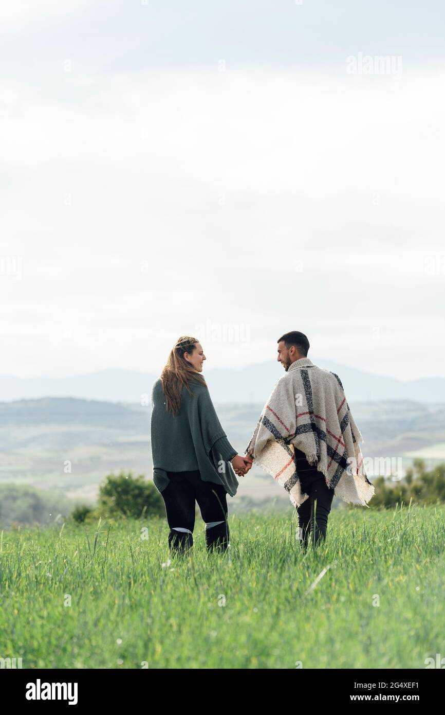 Jeune couple tenant les mains tout en marchant ensemble sur le terrain Banque D'Images Jeune couple tenant les mains tout en marchant ensemble sur le terrain Banque D'Images