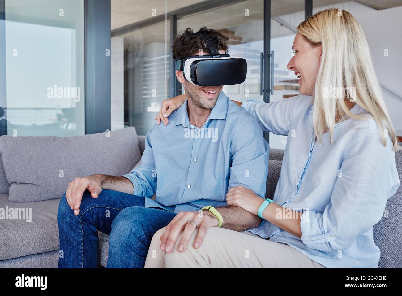 Femme gaie avec le bras autour de regarder l'homme portant le simulateur de réalité virtuelle dans le salon Banque D'Images