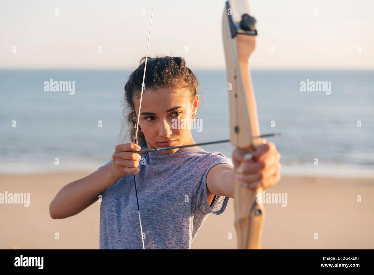 Jeune femme pratiquant le tir à l'arc à la plage Banque D'Images