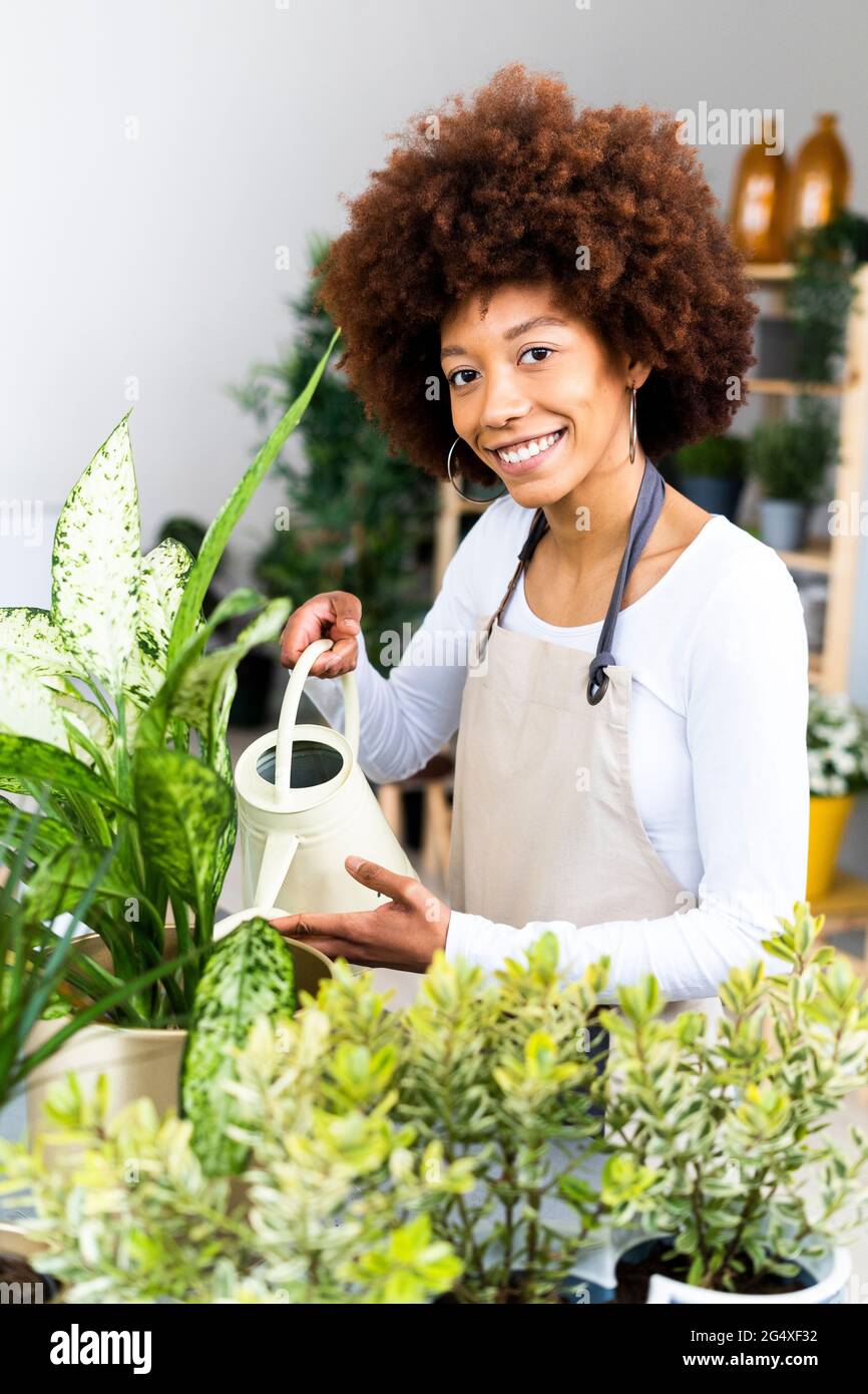 Une jeune fleuriste féminine arrose des plantes en magasin Banque D'Images