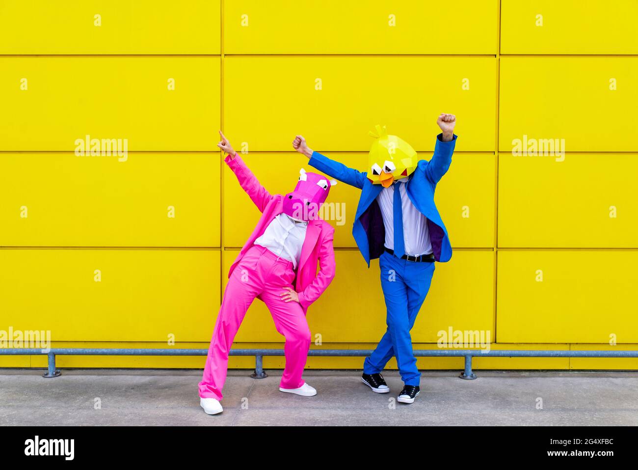 Homme et femme portant des costumes vibrants et des masques d'animaux dansant devant le mur jaune Banque D'Images