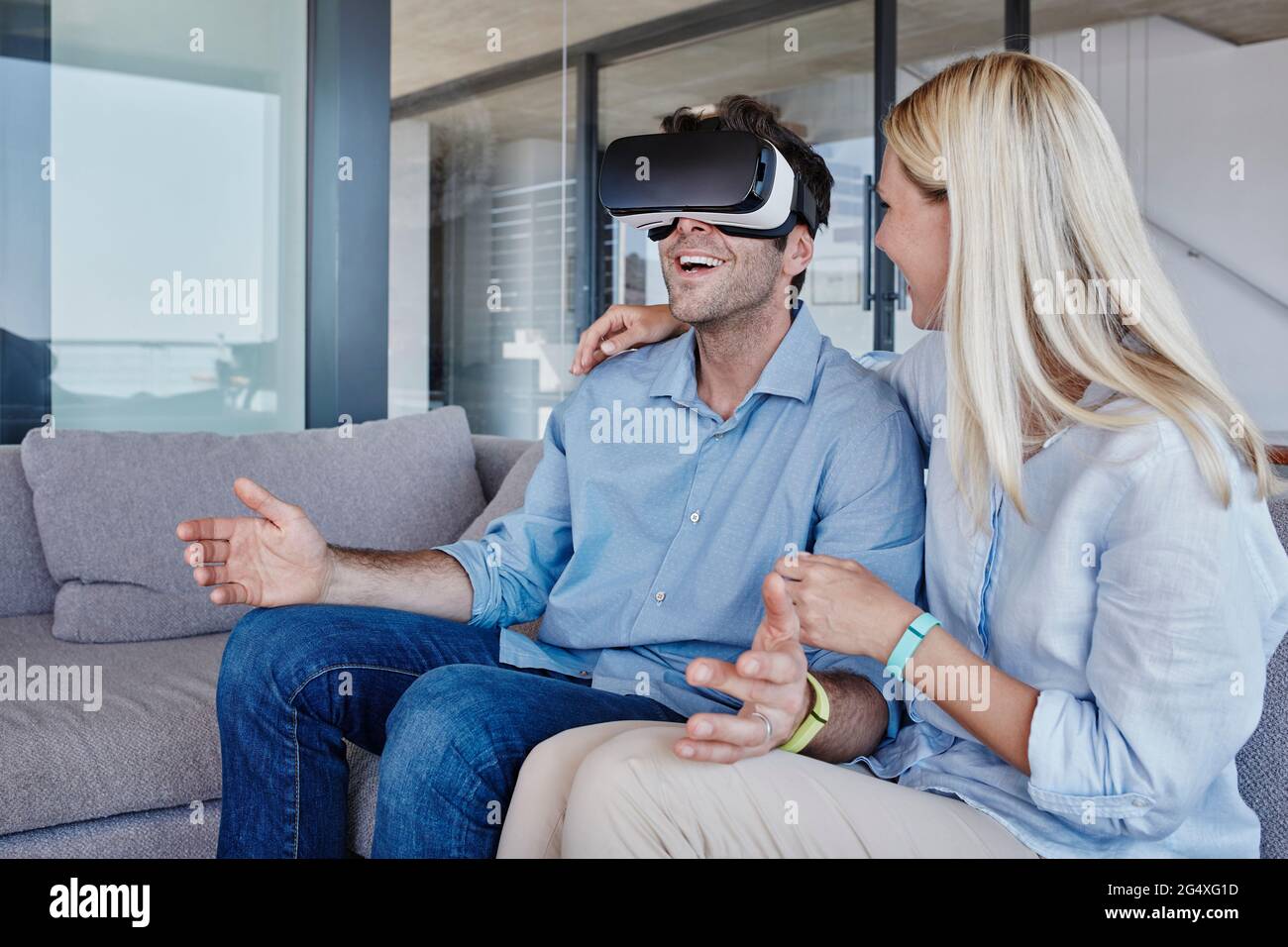 Femme blonde avec le bras autour de regarder l'homme gai portant le simulateur de réalité virtuelle dans le salon Banque D'Images