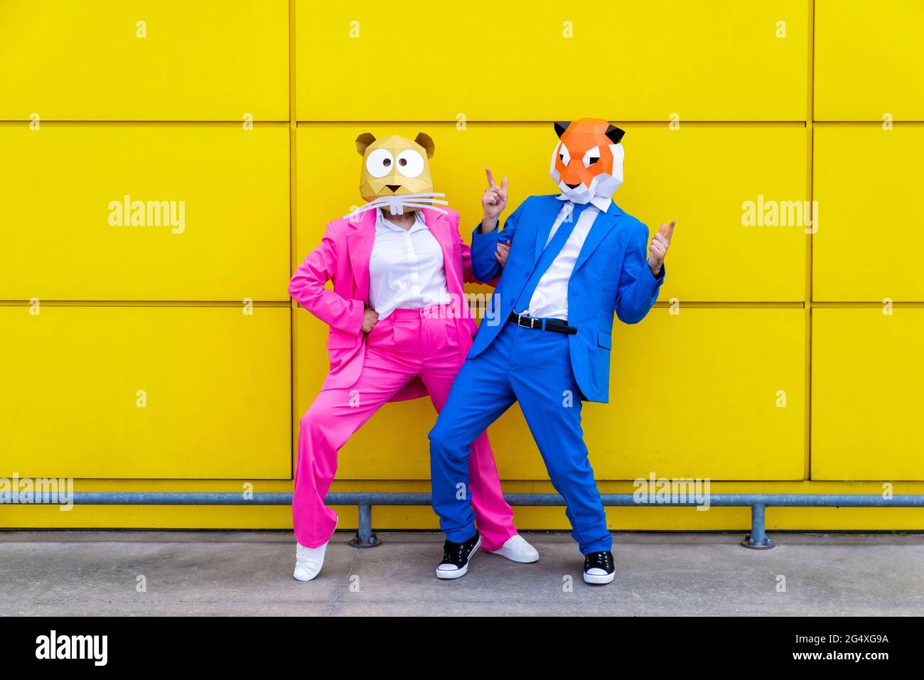 Homme et femme portant des costumes vibrants et des masques pour animaux se posant ensemble contre le mur jaune Banque D'Images