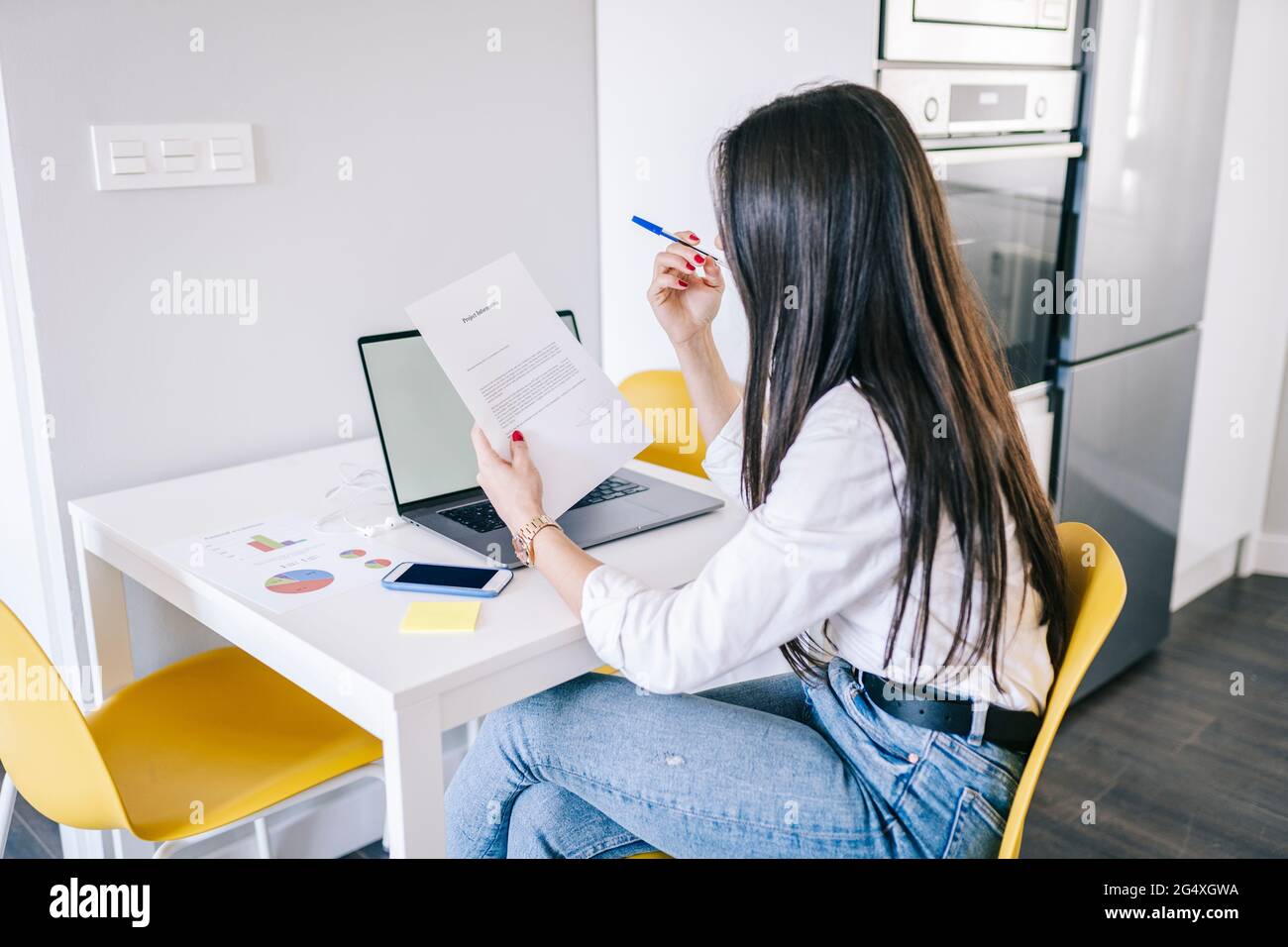 Jeune femme travailleur indépendant qui lit des documents lorsqu'elle est au bureau à domicile Banque D'Images