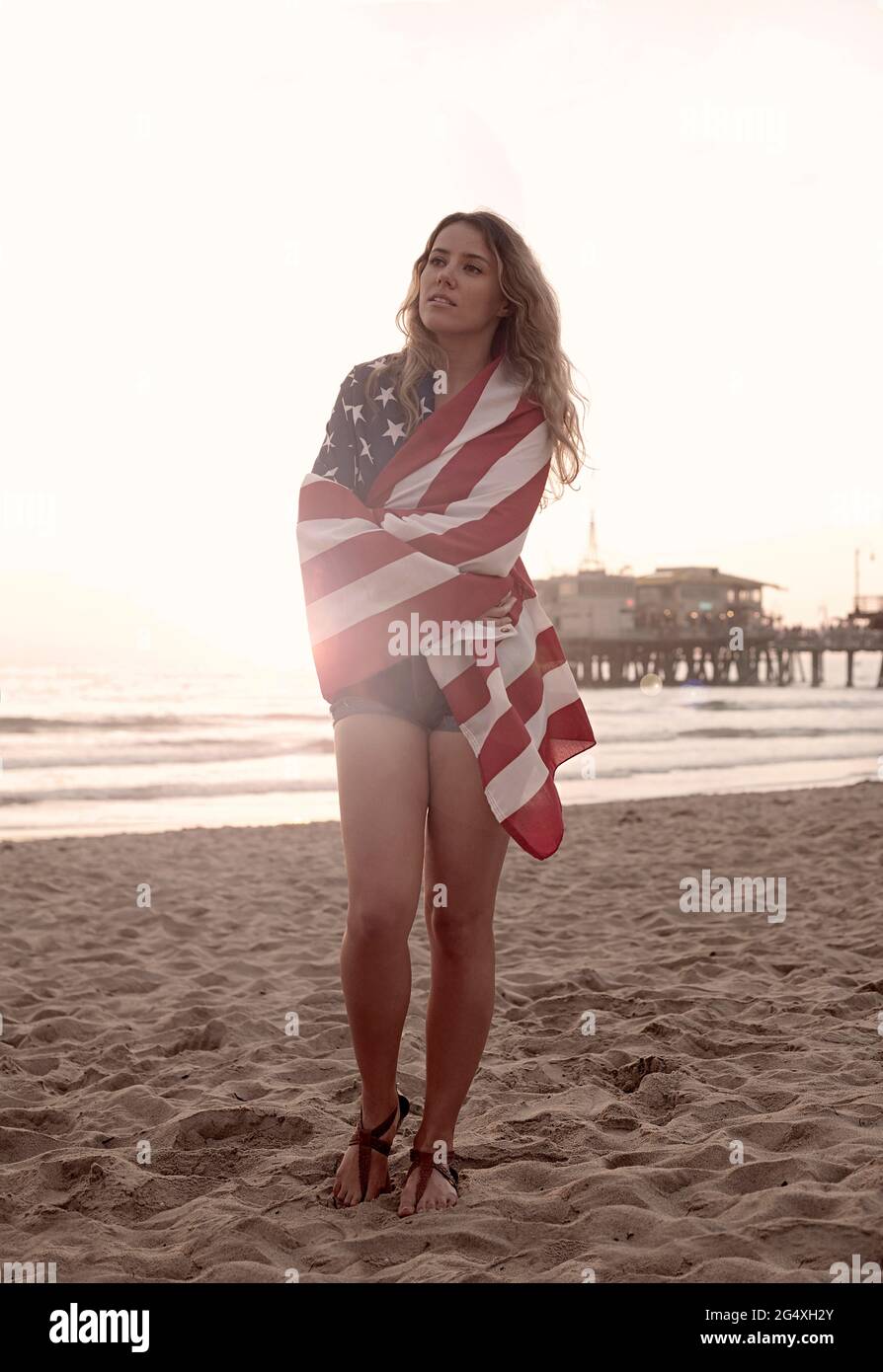 Belle femme enveloppée dans le drapeau en se tenant sur la plage de Santa Monica Banque D'Images