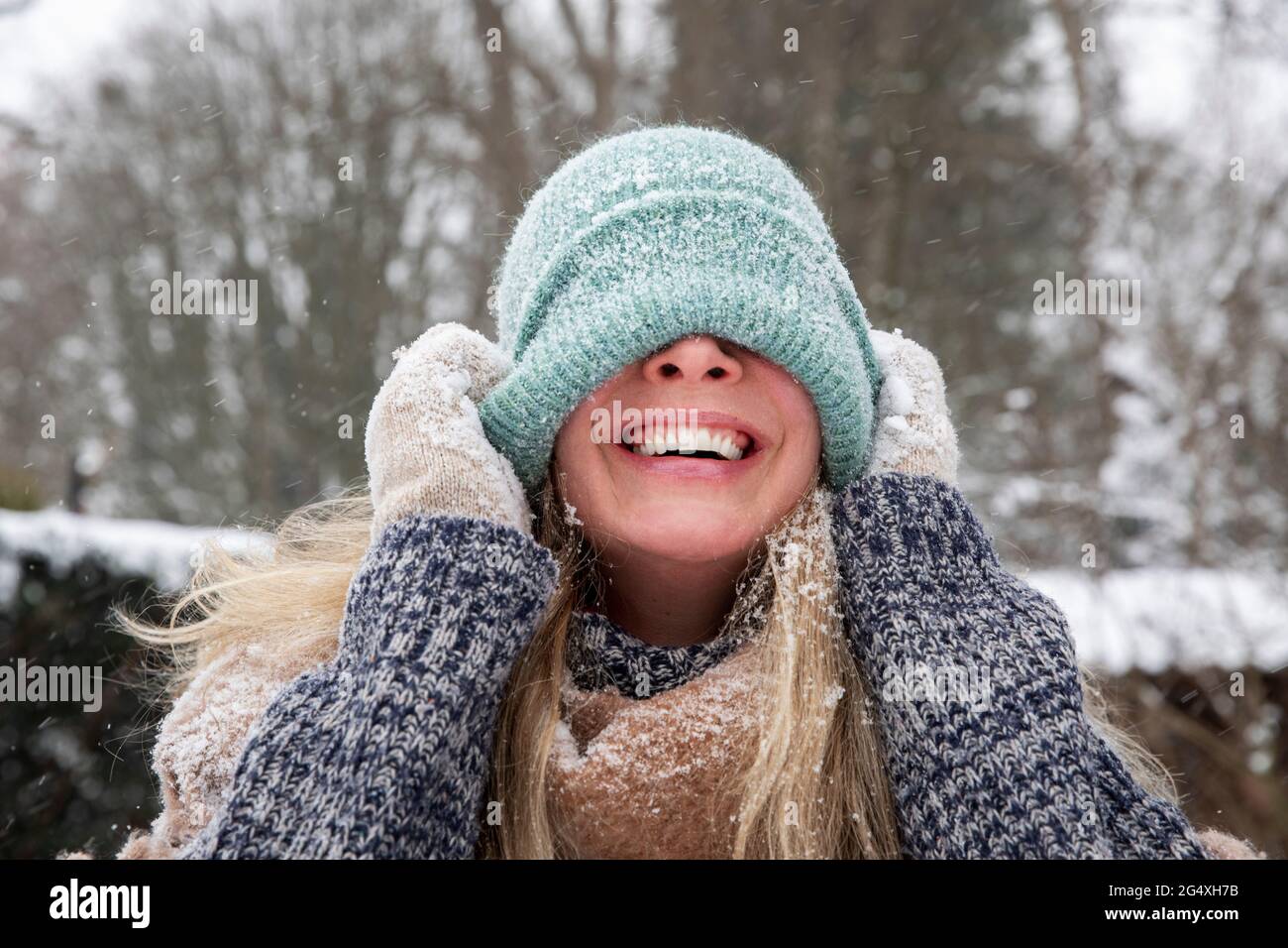 Femme gaie couvrant le visage avec un chapeau en tricot pendant l'hiver Banque D'Images